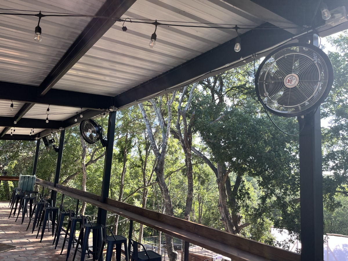 Big Tex misting fans cooling the covered upper deck at Solstice in Jonestown, overlooking the oak tree line